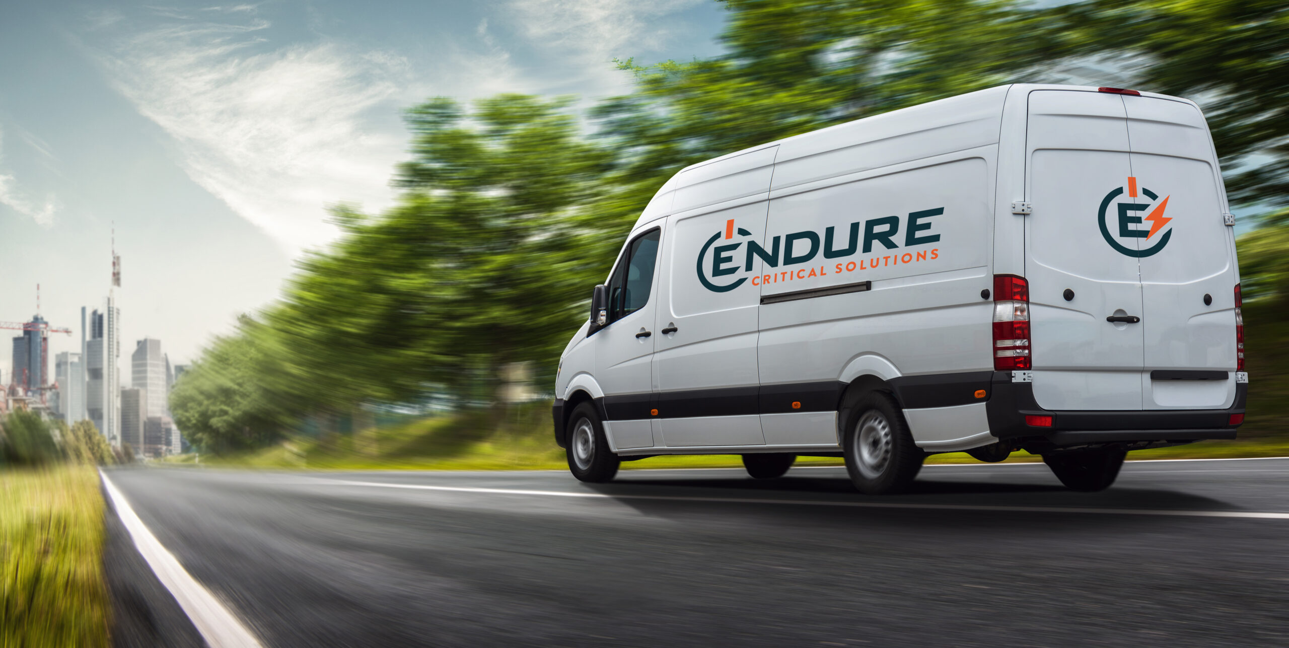 White Endure Critical Solutions van driving on a road with blurred trees and city skyline.
