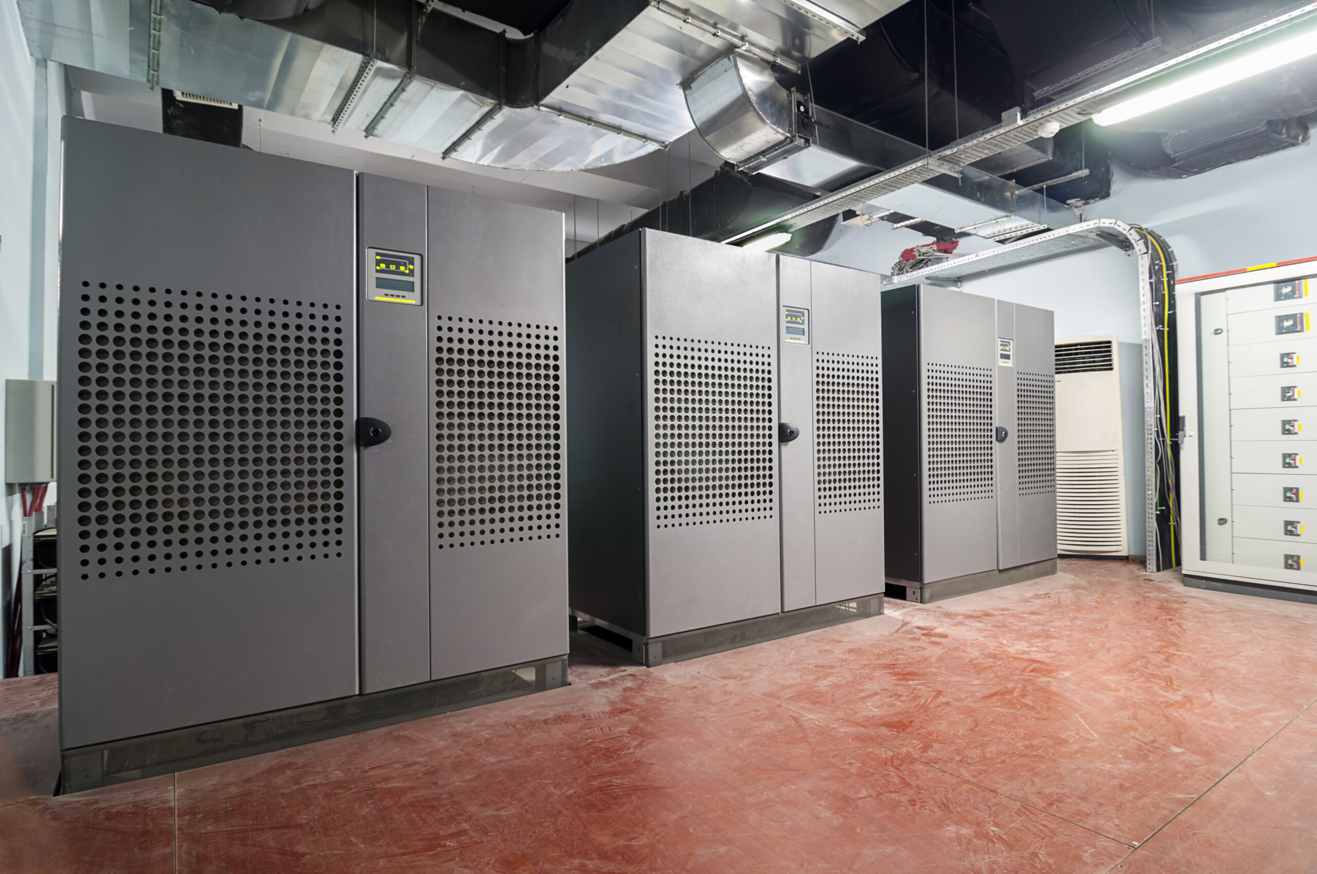 Row of large, gray server cabinets with perforated doors, under ductwork.