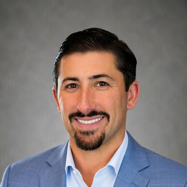 Man with dark hair, mustache, and goatee smiles in a blue suit.